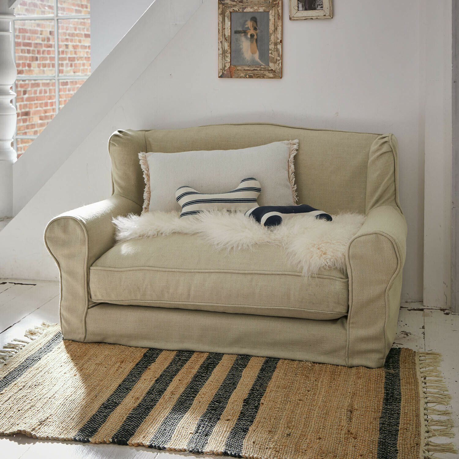 Beiges Zweisitzer-Sofa aus Stoff mit dekorativen Kissen und Fellüberwurf auf Jute-Teppich