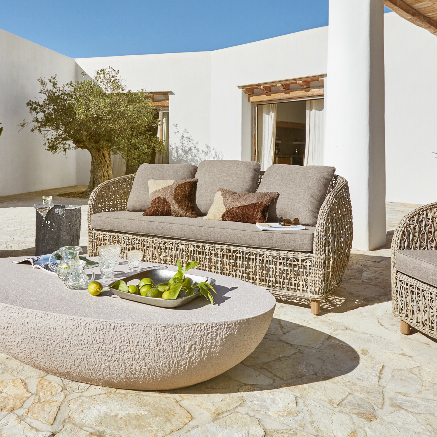 Outdoor-Möbelset mit beigem Rattansofa und ovalem Steintisch mit grünen Früchten auf Terrasse