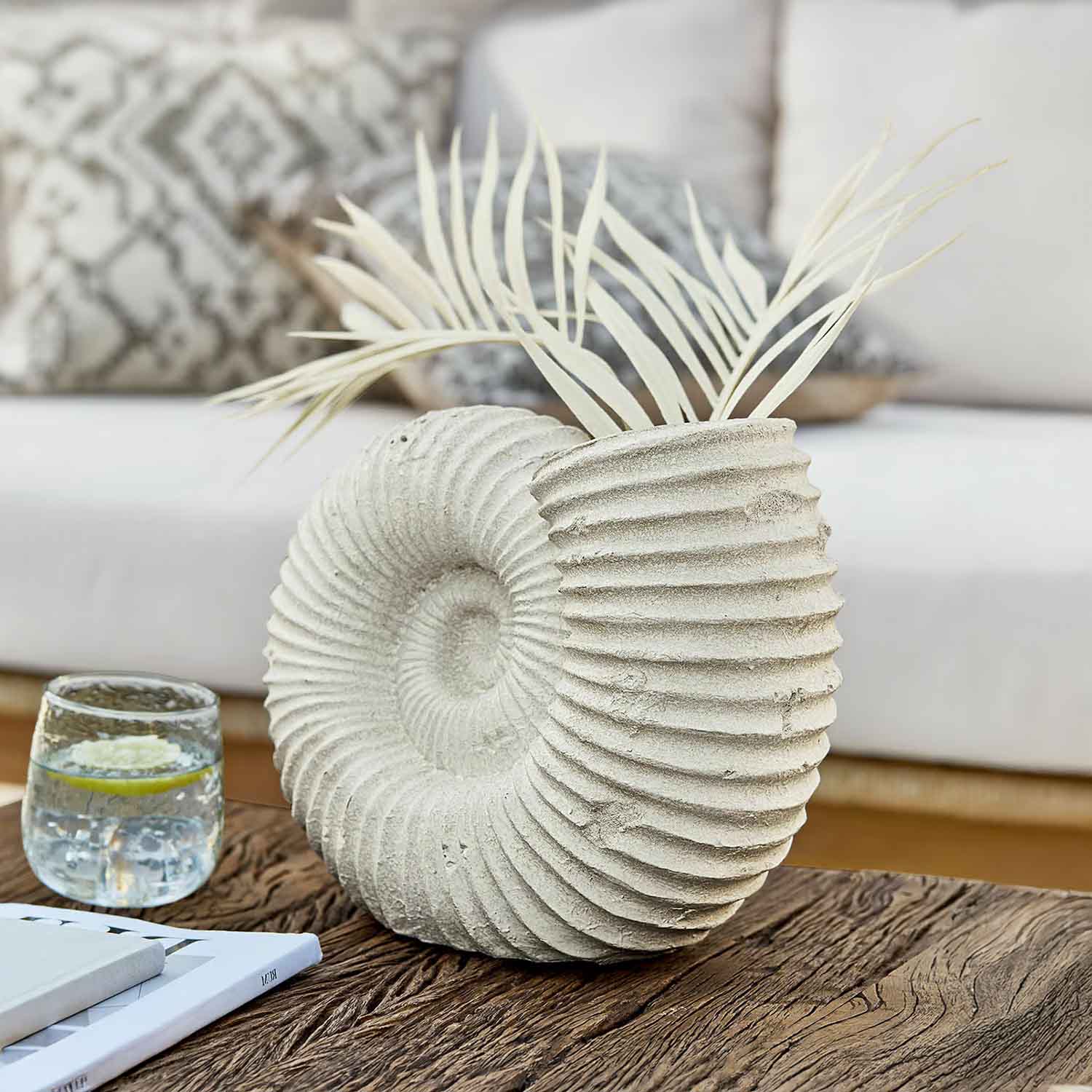 Dekorativer hellsteinfarbener Muschel-Vase mit getrockneten Blättern auf Holztisch