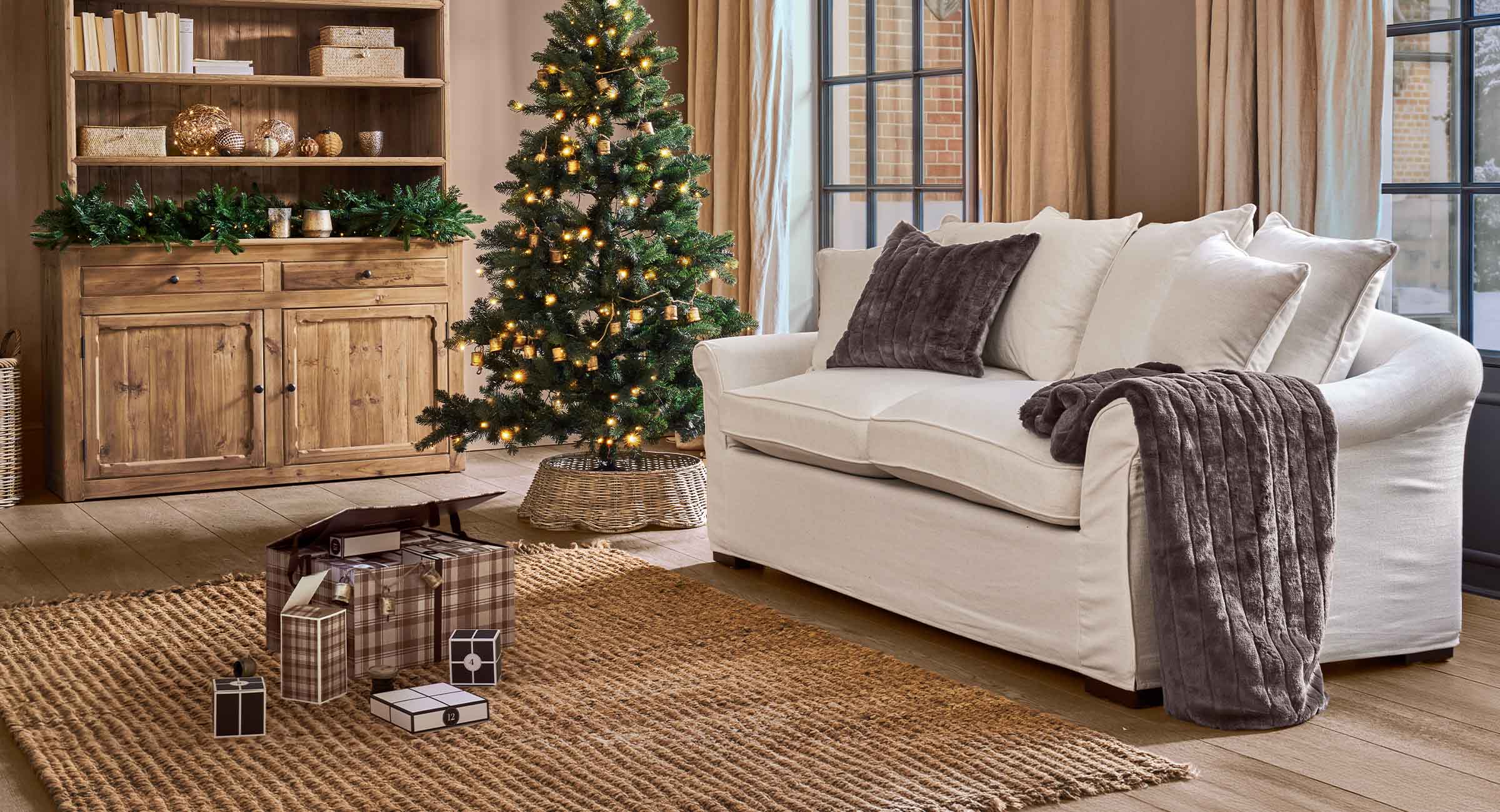 Gemütliches Wohnzimmer mit weißem Sofa, braunen Kissen und beleuchtetem Christbaum