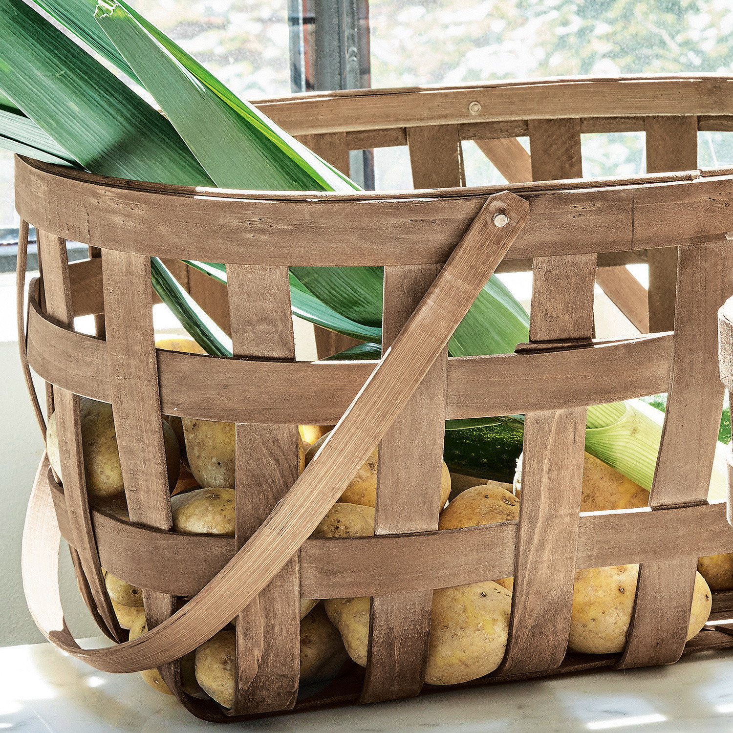 Holzkorb mit Griff gefüllt mit Kartoffeln und grünen Blättern auf Küchenarbeitsplatte