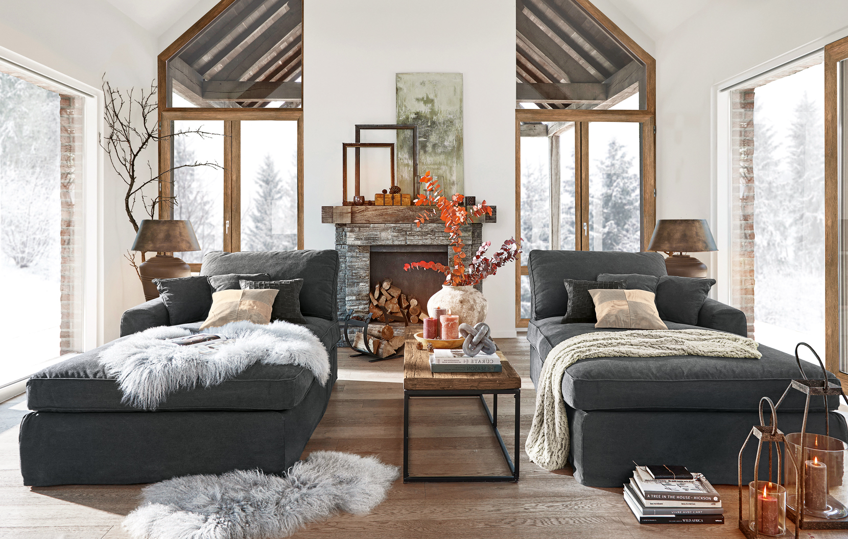 Gemütliches Landhaus-Wohnzimmer mit zwei dunkelgrauen Sofas und steinernem Kamin im Hintergrund