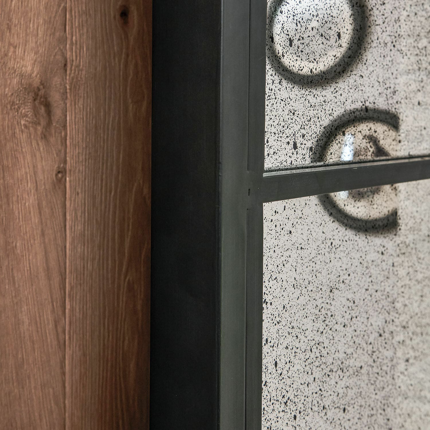 Schwarzer Metallrahmen mit dekorativ gealtertem Spiegel und Holzwand im Hintergrund