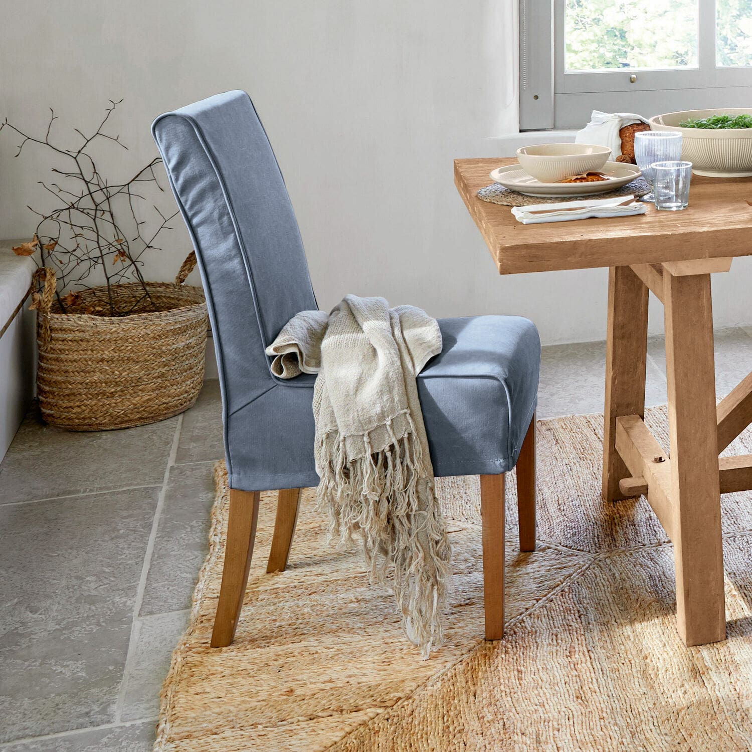 Stuhl mit Husse Mankato Blau gepolsterter Stuhl mit Holzbeinen und beigem Plaid neben hellem Holztisch