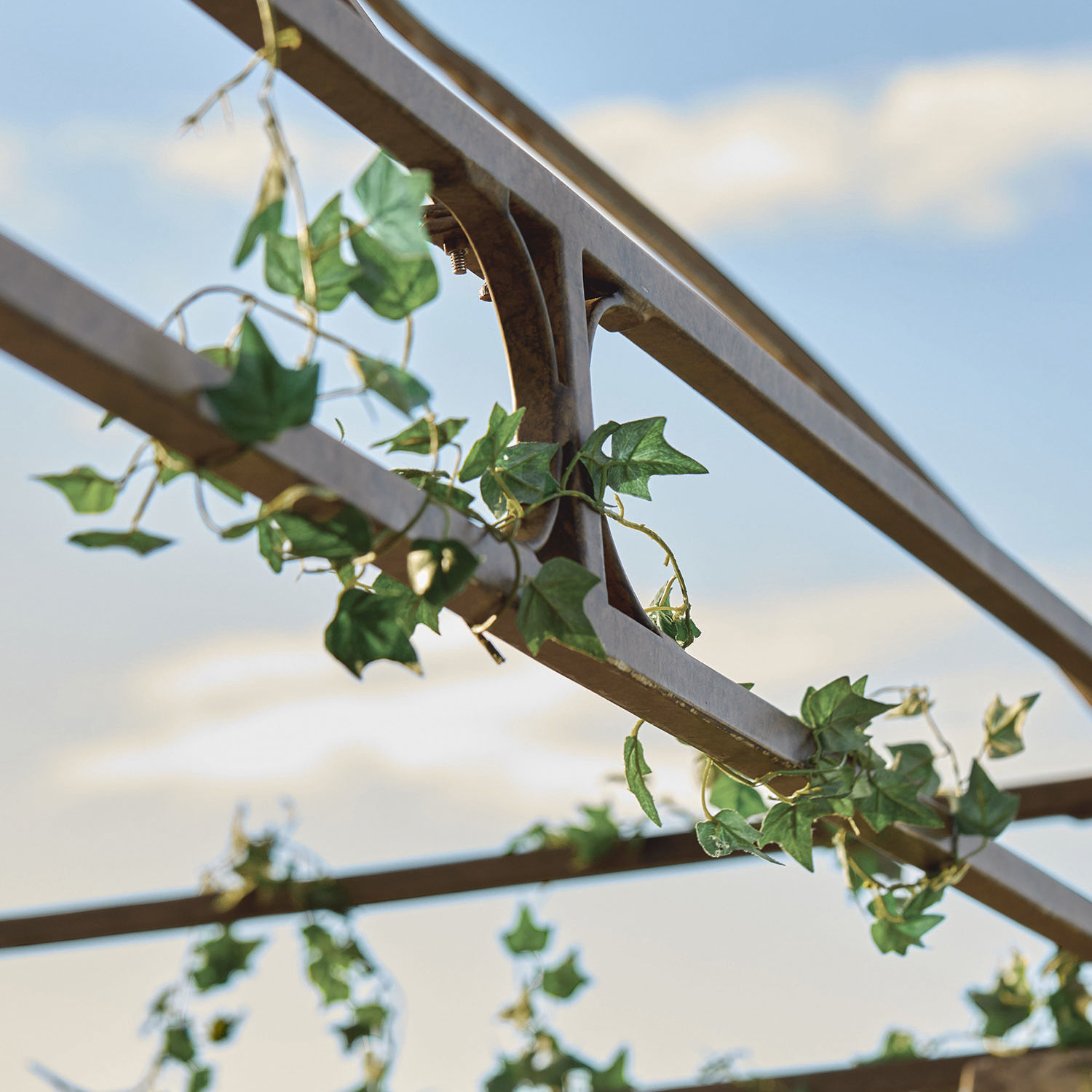 Metallgestell einer rostfarbenen Pergola mit grünem Efeu vor Himmel, Gartendekoration