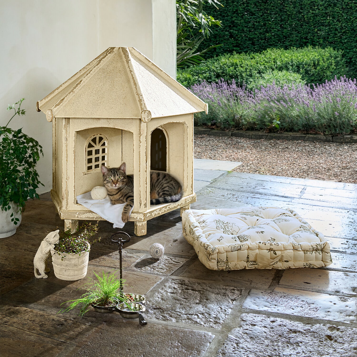 Beiges Metall-Katzenhaus mit Kissen und Spielzeug auf Steinboden im Garten