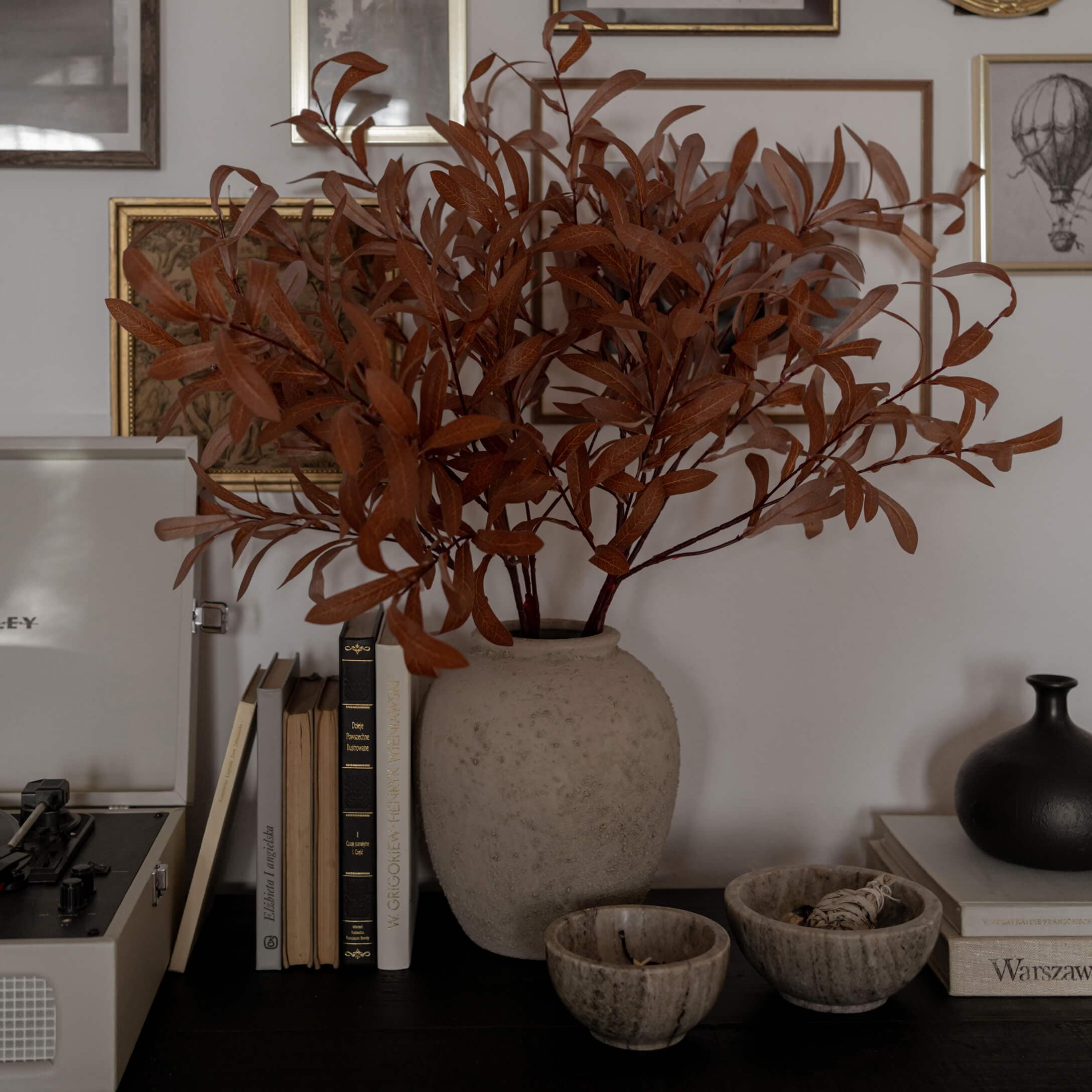 Beige Alabastervase mit getrockneten braunen Zweigen auf dunklem Tisch mit Büchern und Dekoration