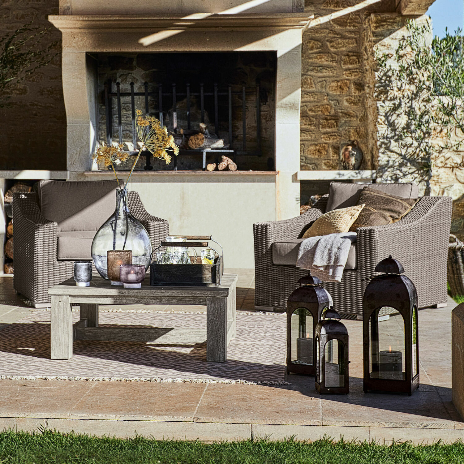 Gartenmöbel-Set mit grauen Polstern und Holztisch auf Terrasse mit dekorativen Laternen