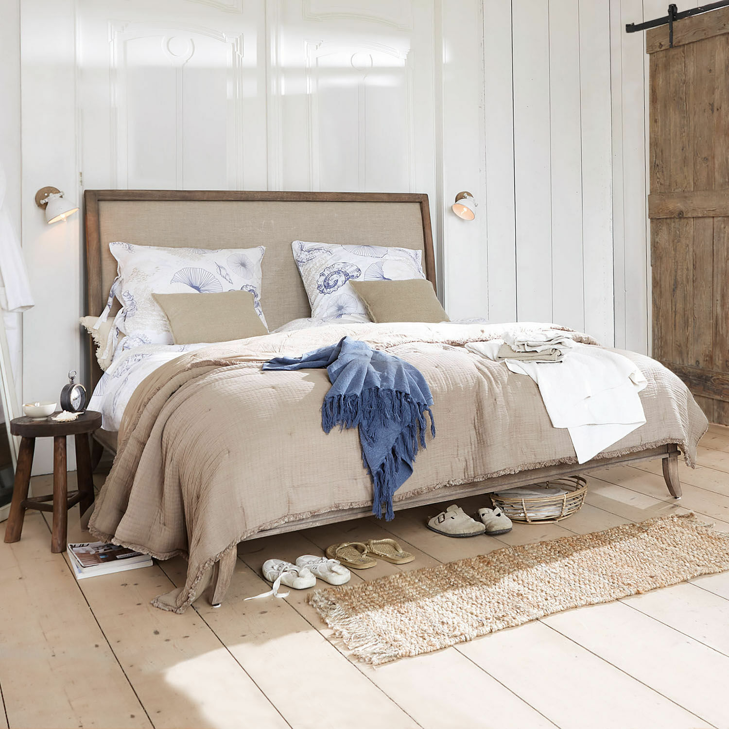 Holzrahmenbett mit beiger Bettwäsche in hellem Schlafzimmer im natürlichen Landhausstil