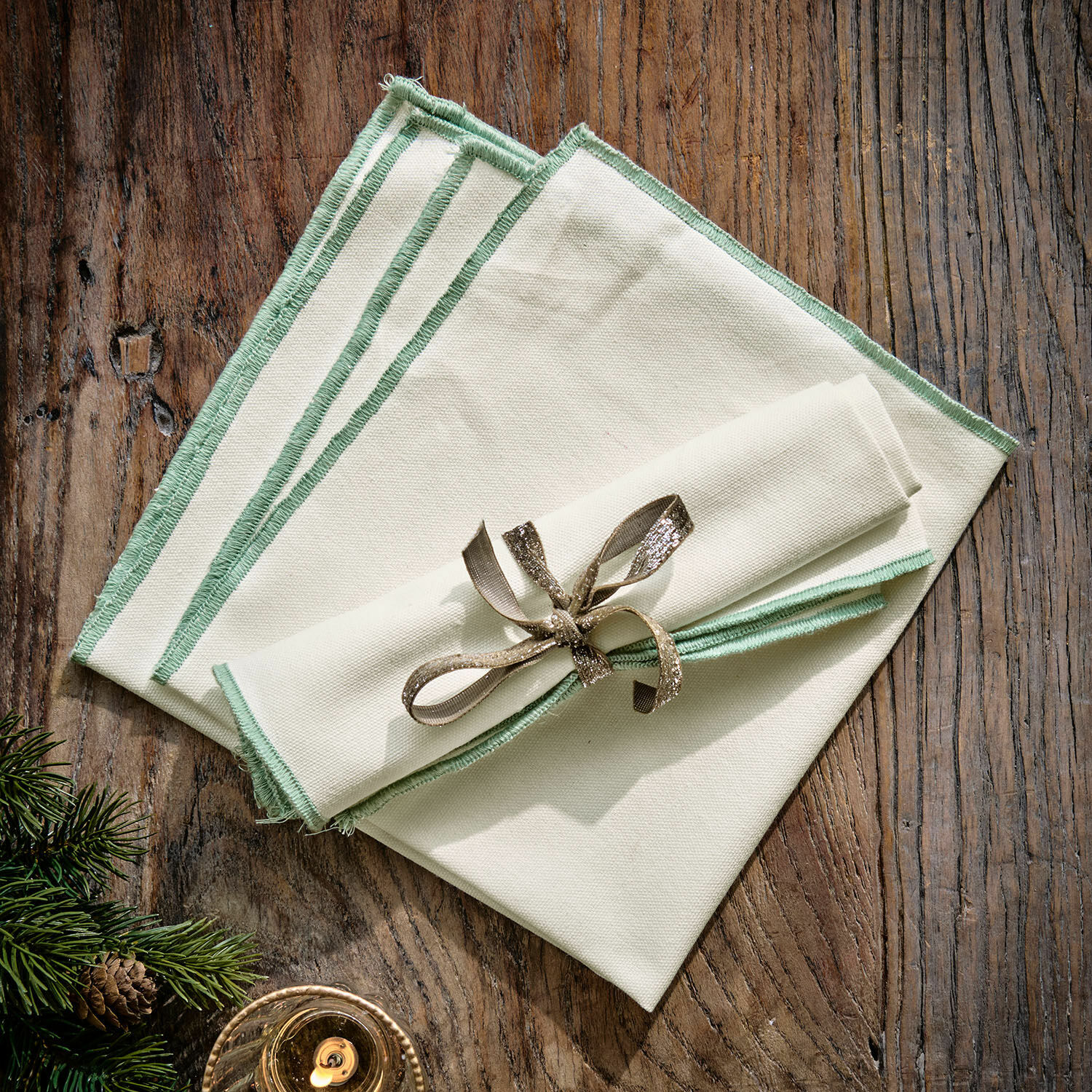 Serviette 2er Set Tarivelle Set aus cremefarbenen Leinenservietten mit grünem Saum auf Holztisch, festliche Dekoration