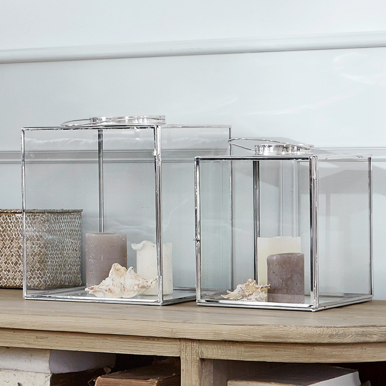 Zwei Glaslaternen mit silbernem Metallrahmen, Kerzen und Muscheln auf einem Holztisch