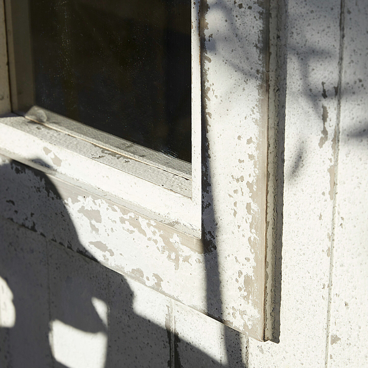 Nahaufnahme eines weißen, verwitterten Fensterrahmens mit abblätternder Farbe an Außenwand