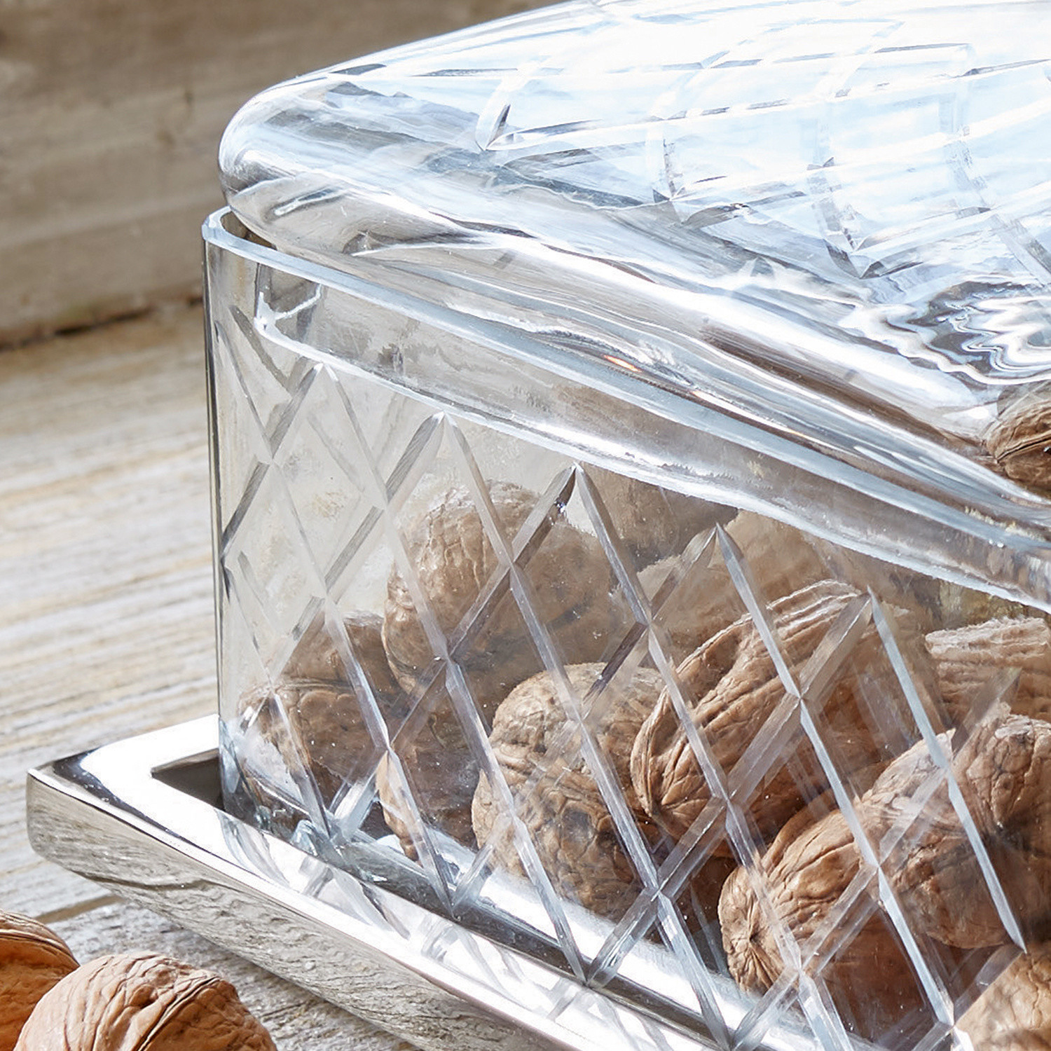 Transparentes Glasbehälter mit Deckel und Rautenmuster, gefüllt mit Walnüssen auf Metalltablett
