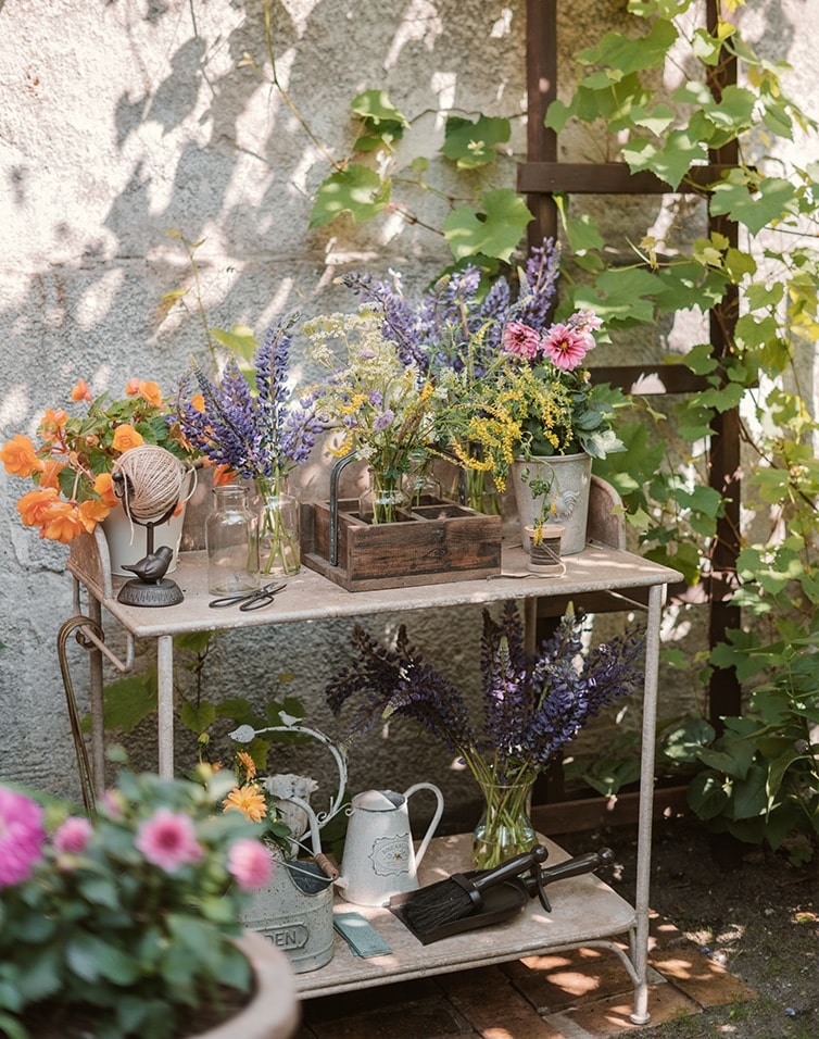 Metall-Gartentisch mit Blumen und Gartengeräten an sonnigem, schattigem Platz
