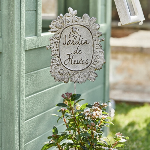 Metall-Gartendekoration mit Schriftzug Jardin de Fleurs vor grünem Hintergrund