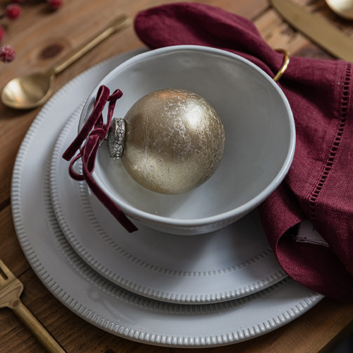 Weißes Keramik-Teller-Set mit bordeauxrotem Stoffserviette und goldener Kugel auf Holztisch