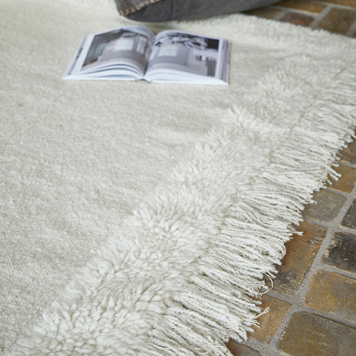 Weißer Teppich mit weichem Fransenrand auf Steinboden, gemütliche Wohnraumdekoration
