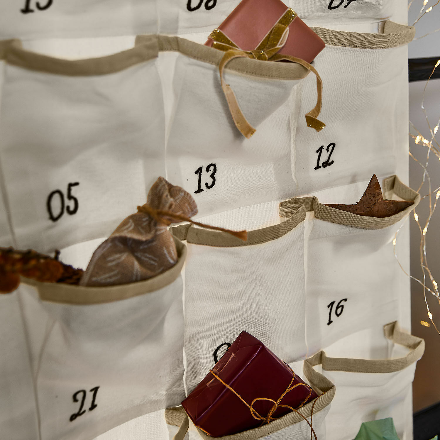 Adventskalender aus weißem Baumwollstoff mit beigen Kanten und schwarzen Zahlen, gefüllt mit kleinen Geschenken