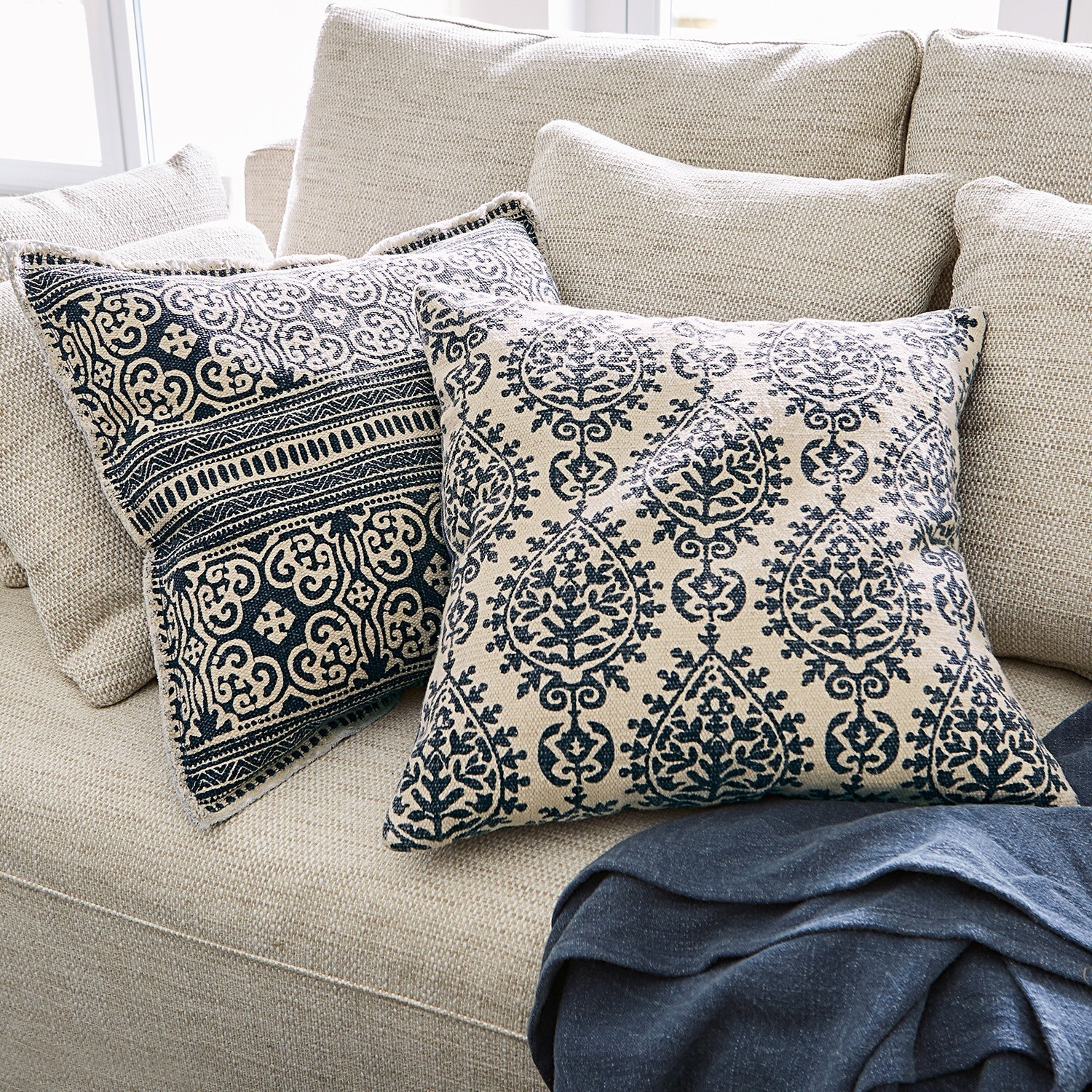 Beiges Sofa mit zwei dekorativen Kissen mit schwarzem Muster und dunkler Decke