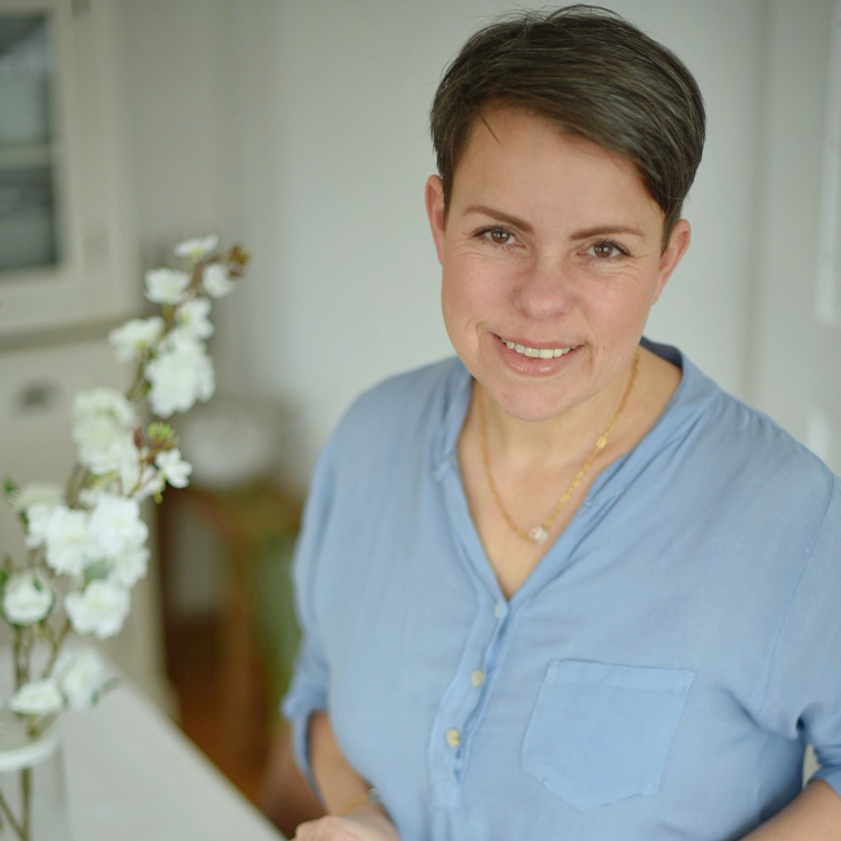 Lächelnde Frau in blauem Hemd neben weißen Blumen in hellem Raum