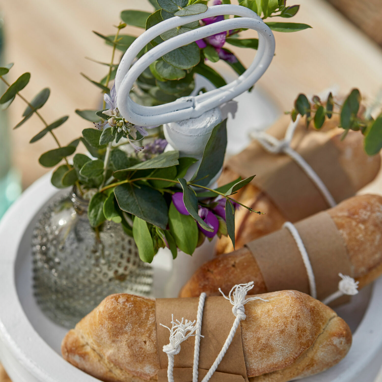 Frisches Brot in Papier und Schnur auf weißem Tablett mit grüner Blatt- und lila Blumendekoration