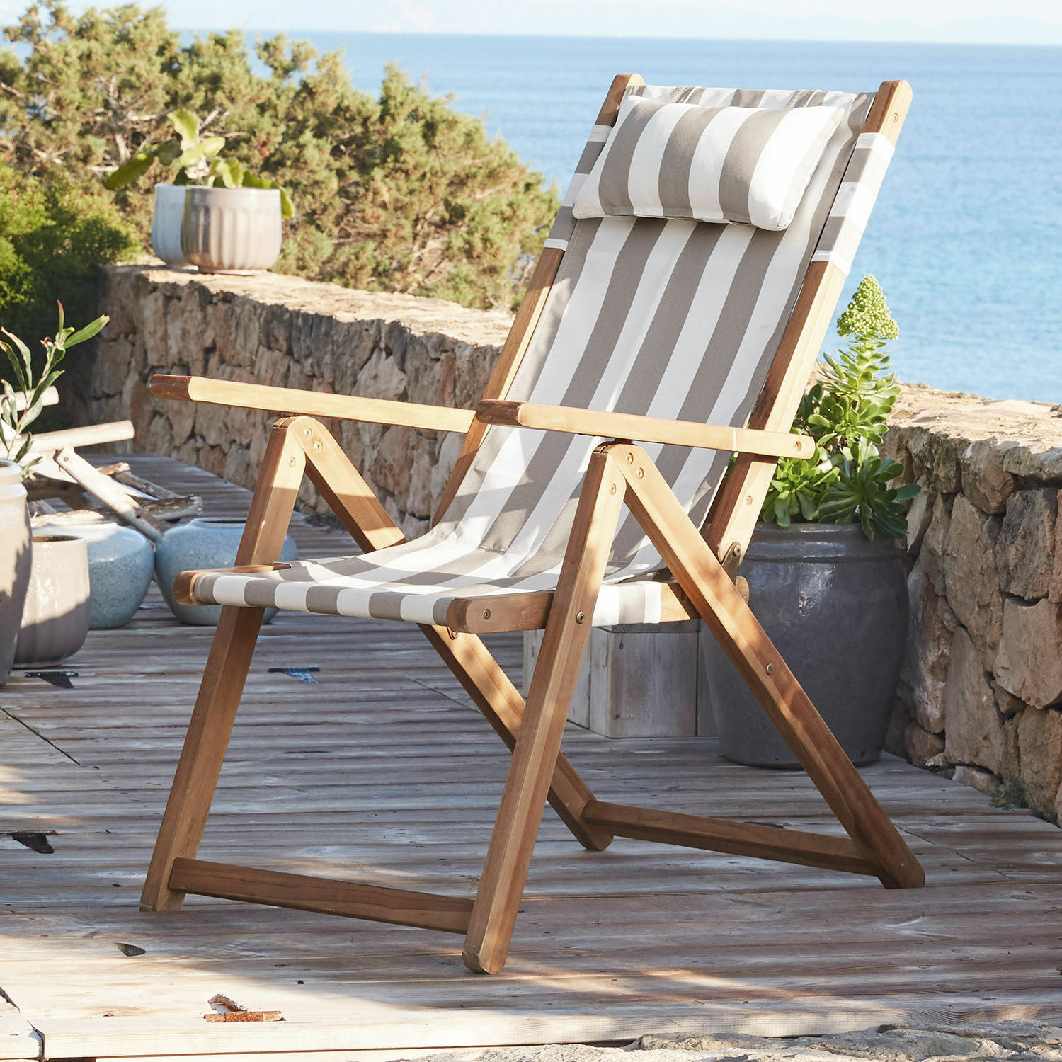 Liegestuhl aus Teakholz mit beige-weiß gestreiftem Stoff auf Terrasse mit Meerblick