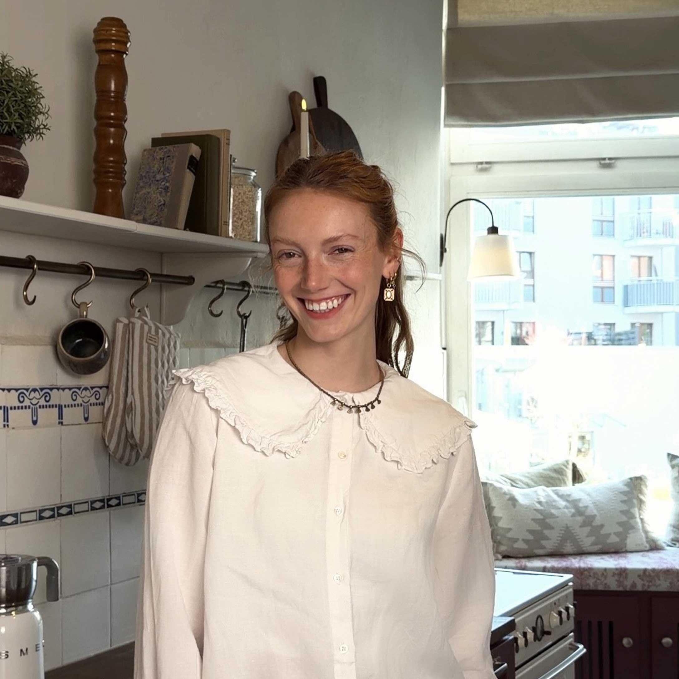Frau in weißer Bluse mit Rüschen in heller Küche mit dekorativen Accessoires und Fenster