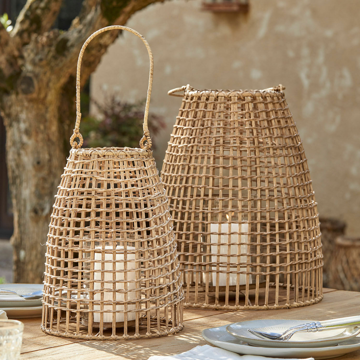 Laterne 2er Set Hillendale Zwei natürliche Rattan-Laternen mit weißen Kerzen auf einem Holztisch im Außenbereich