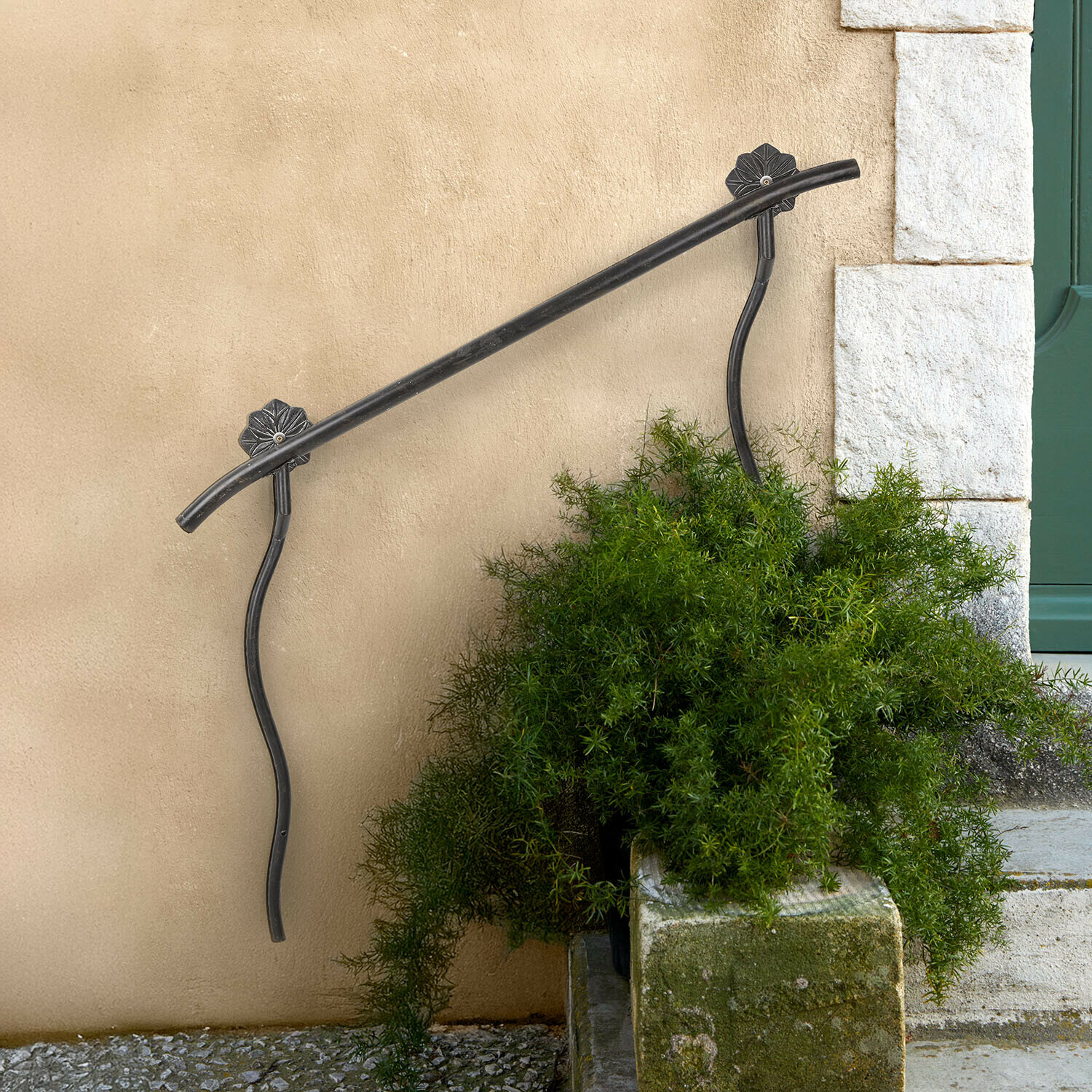 Schwarzes Metallgeländer mit dekorativen Halterungen an beiger Wand neben Treppe mit grünen Pflanzen