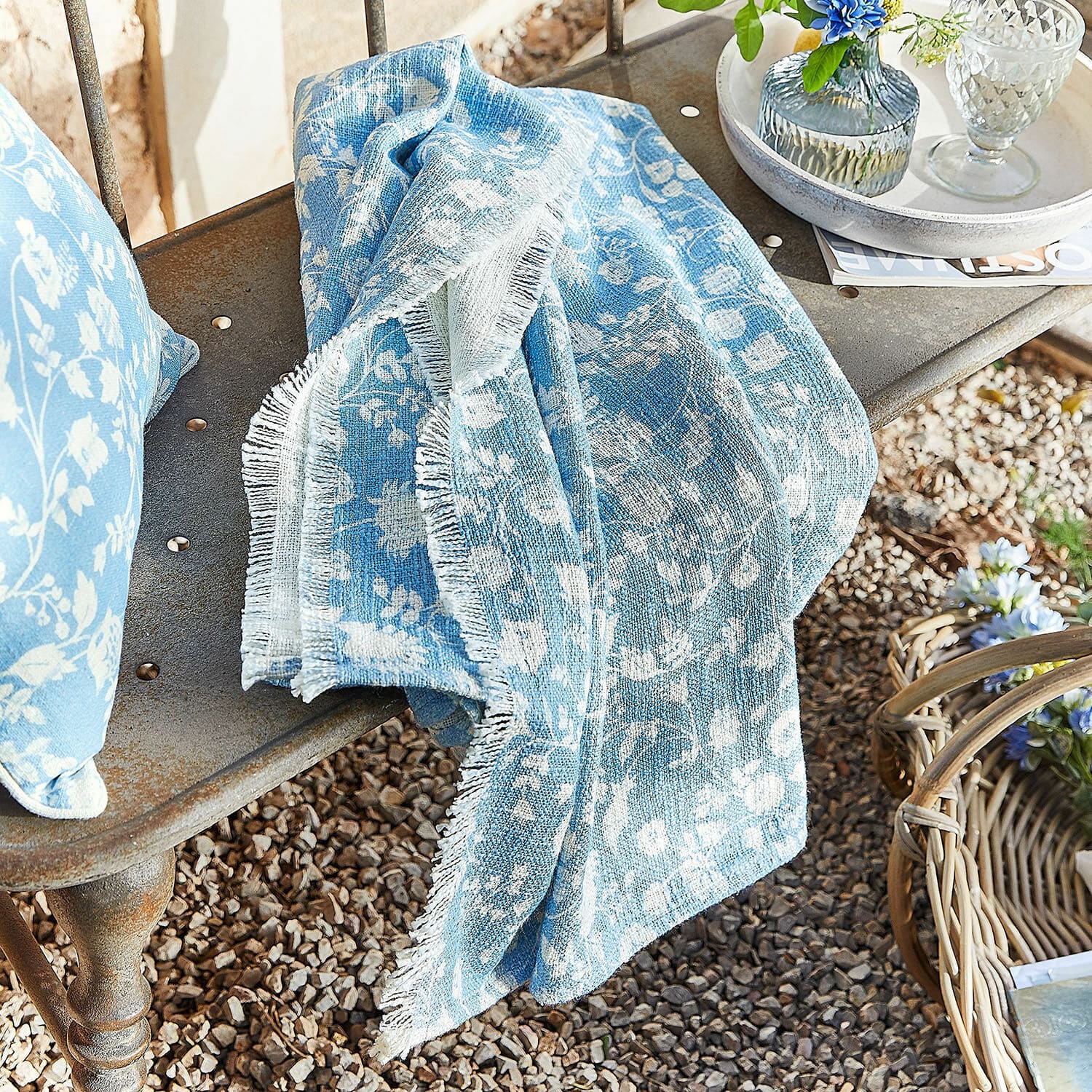 Plaid Corvelique Blaues Baumwollplaid mit weißem Blumenmuster auf Metallbank im Garten drapiert