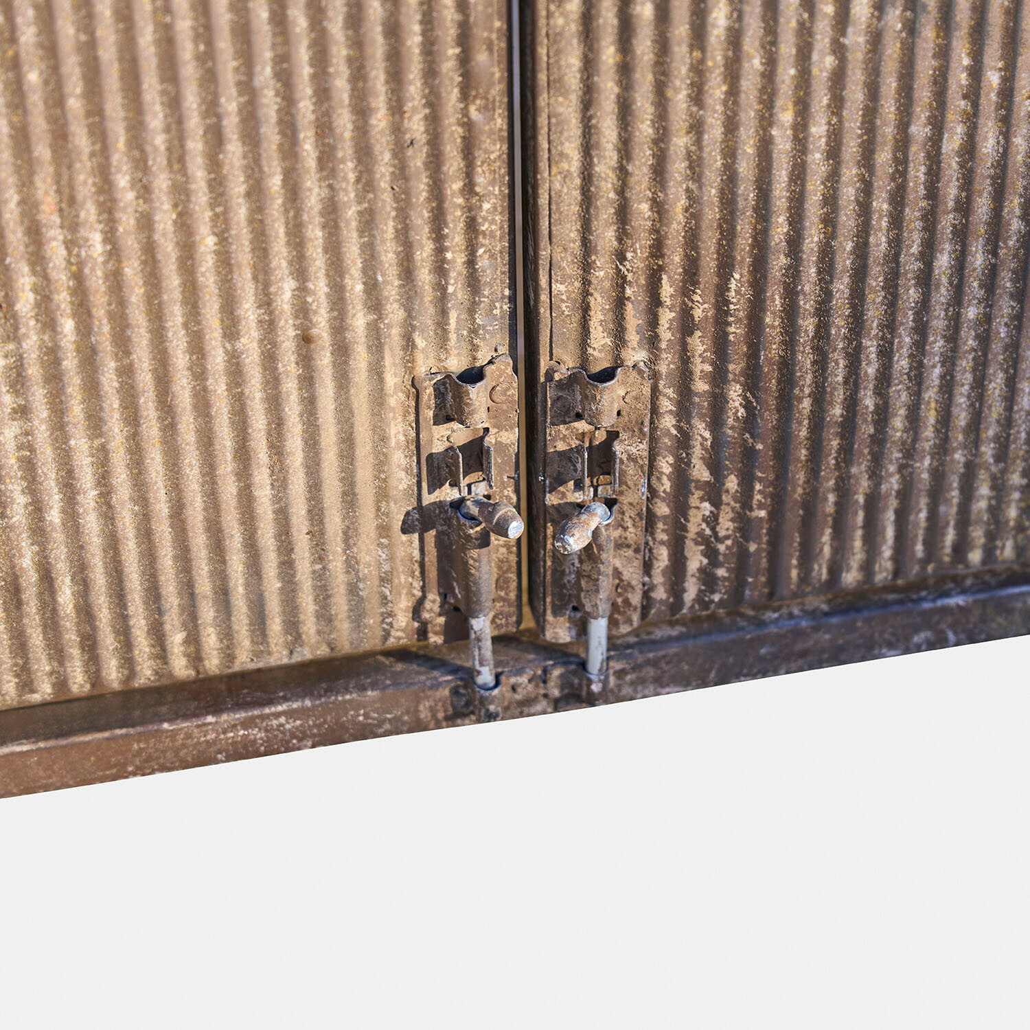 Metallverschluss einer braunen, geriffelten Schranktür mit zwei Riegeln und sichtbarem Gebrauchsspuren