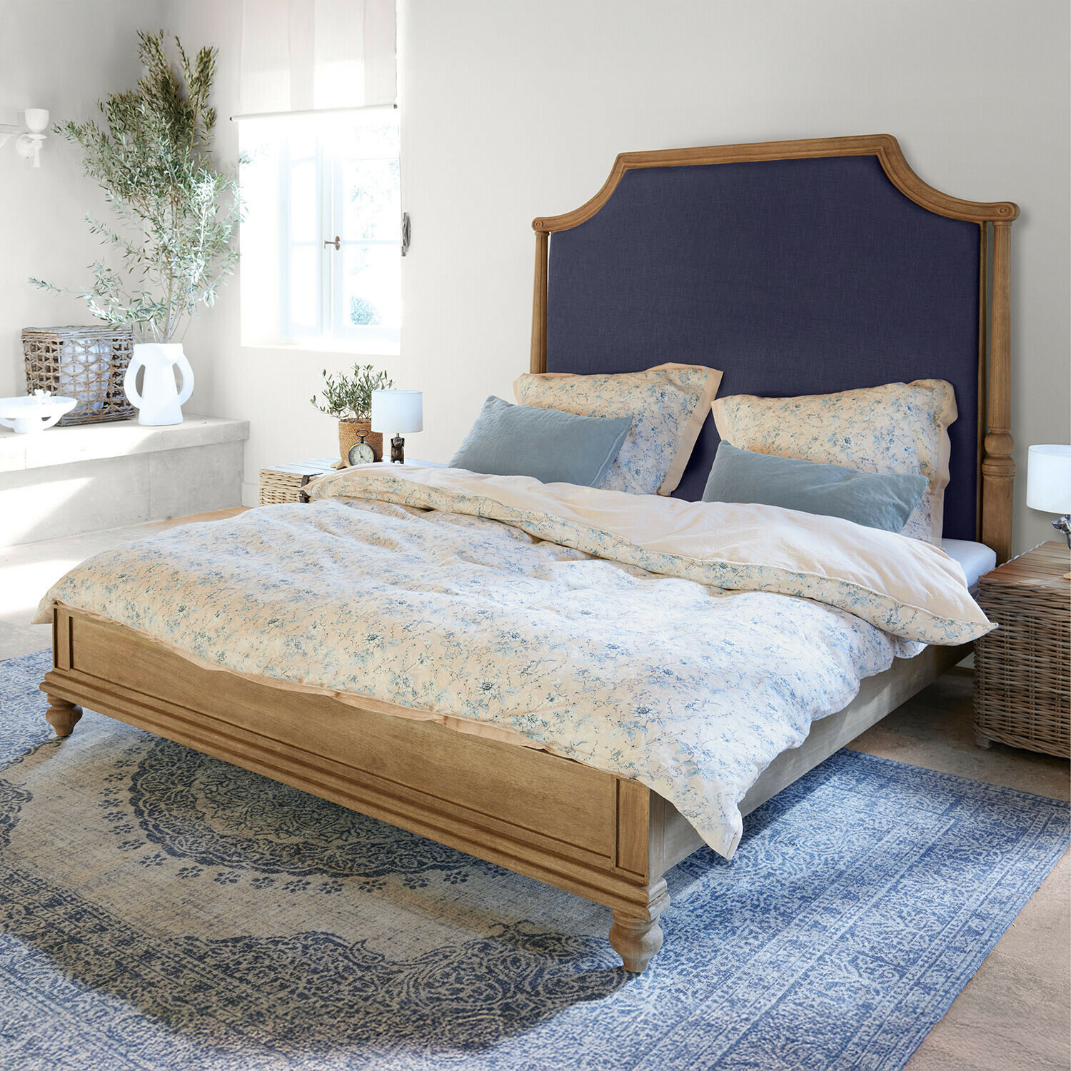 Bett Fairmontine Holzbett mit dunkelblau gepolstertem Kopfteil in hellem Schlafzimmer mit blauem Teppich