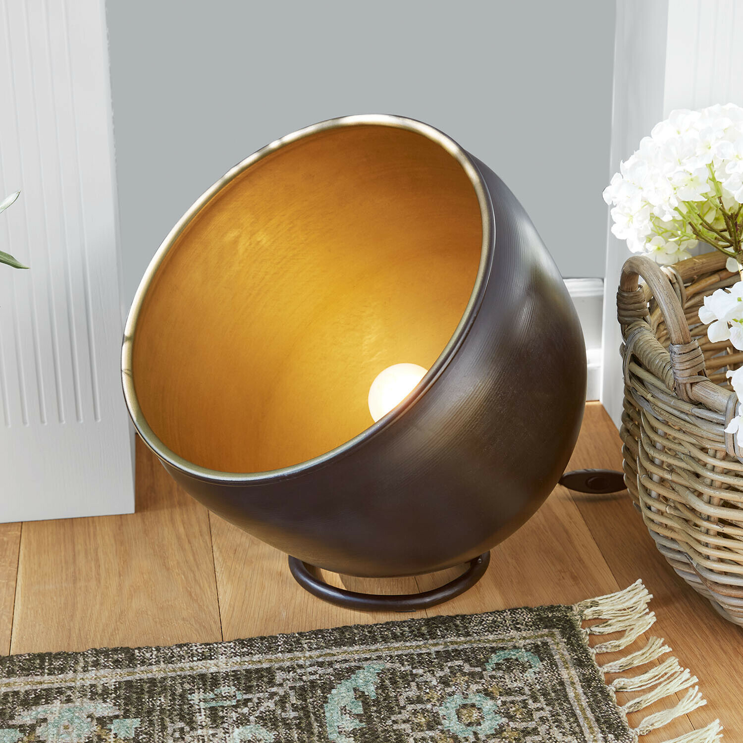 Metall-Tischlampe mit goldfarbenem Innenraum und schwarzer Außenfläche auf Holzboden