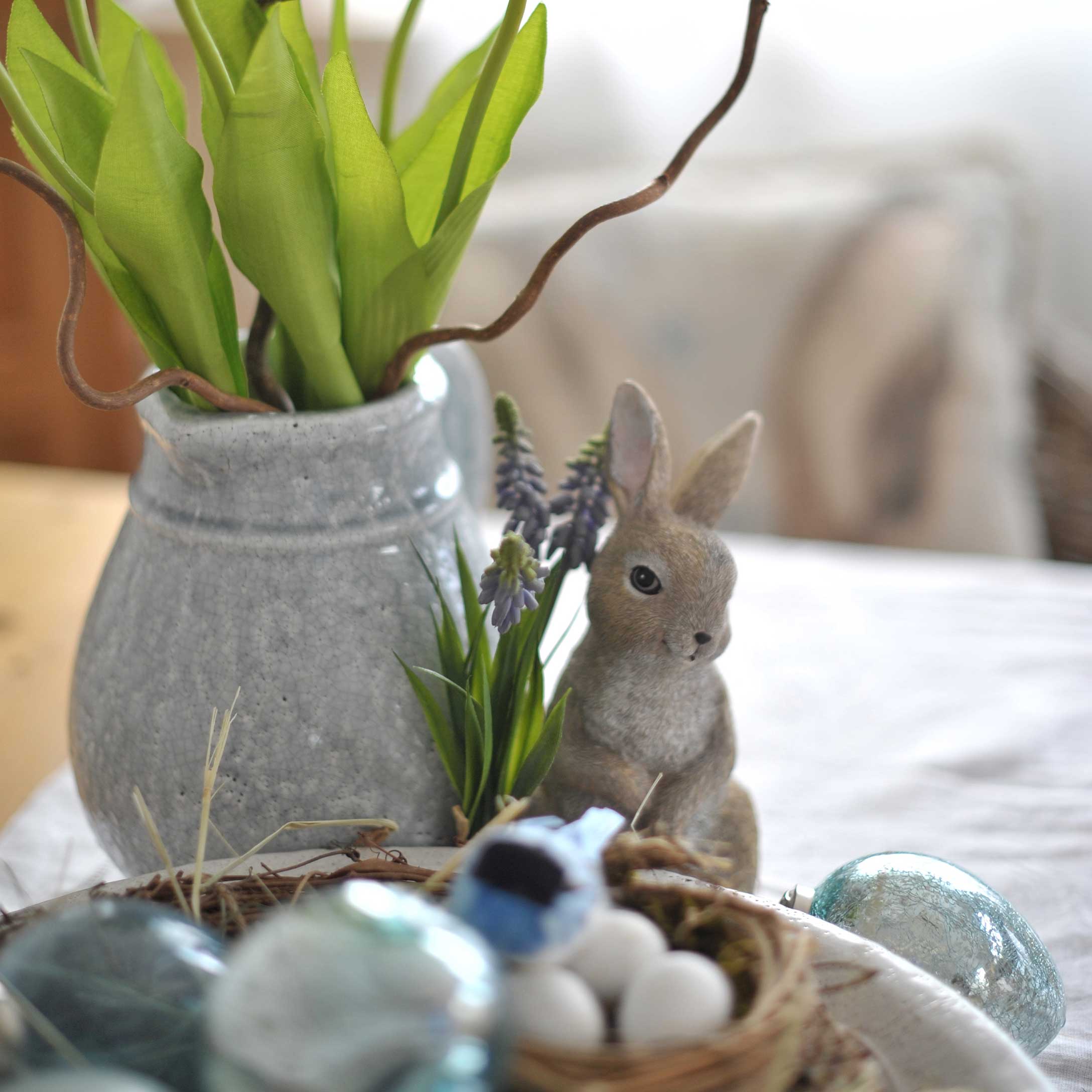 Grauer Keramikvase mit grünen Blättern und Hasenfigur als Osterdekoration auf Tisch