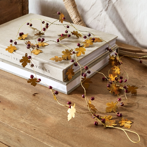 Dekorative Girlande mit goldfarbenen Metallblättern und roten Beeren auf Holztisch