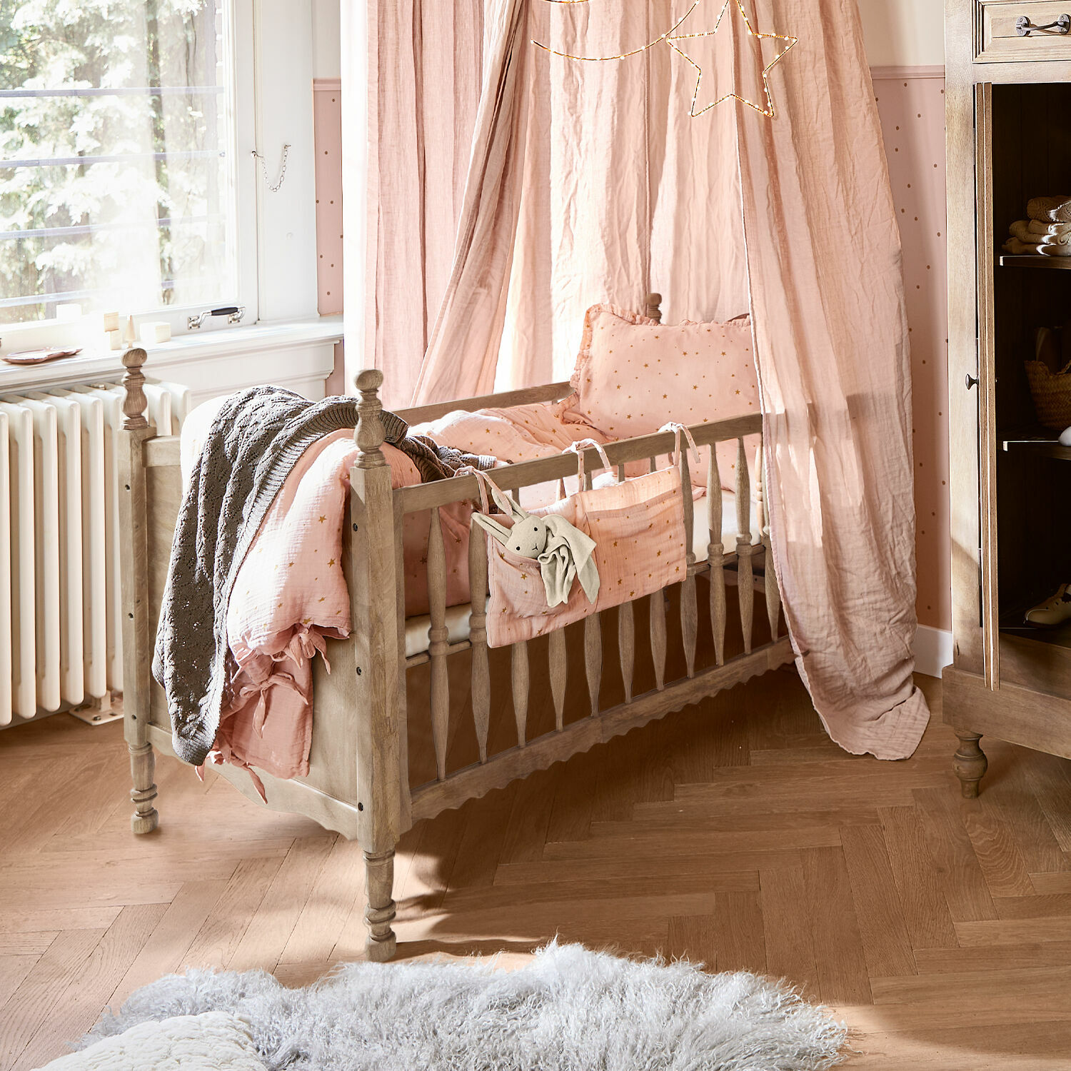 Kinderbett aus Holz mit rosa Baumwollhimmel und Bettwäsche mit Sternmuster im Kinderzimmer