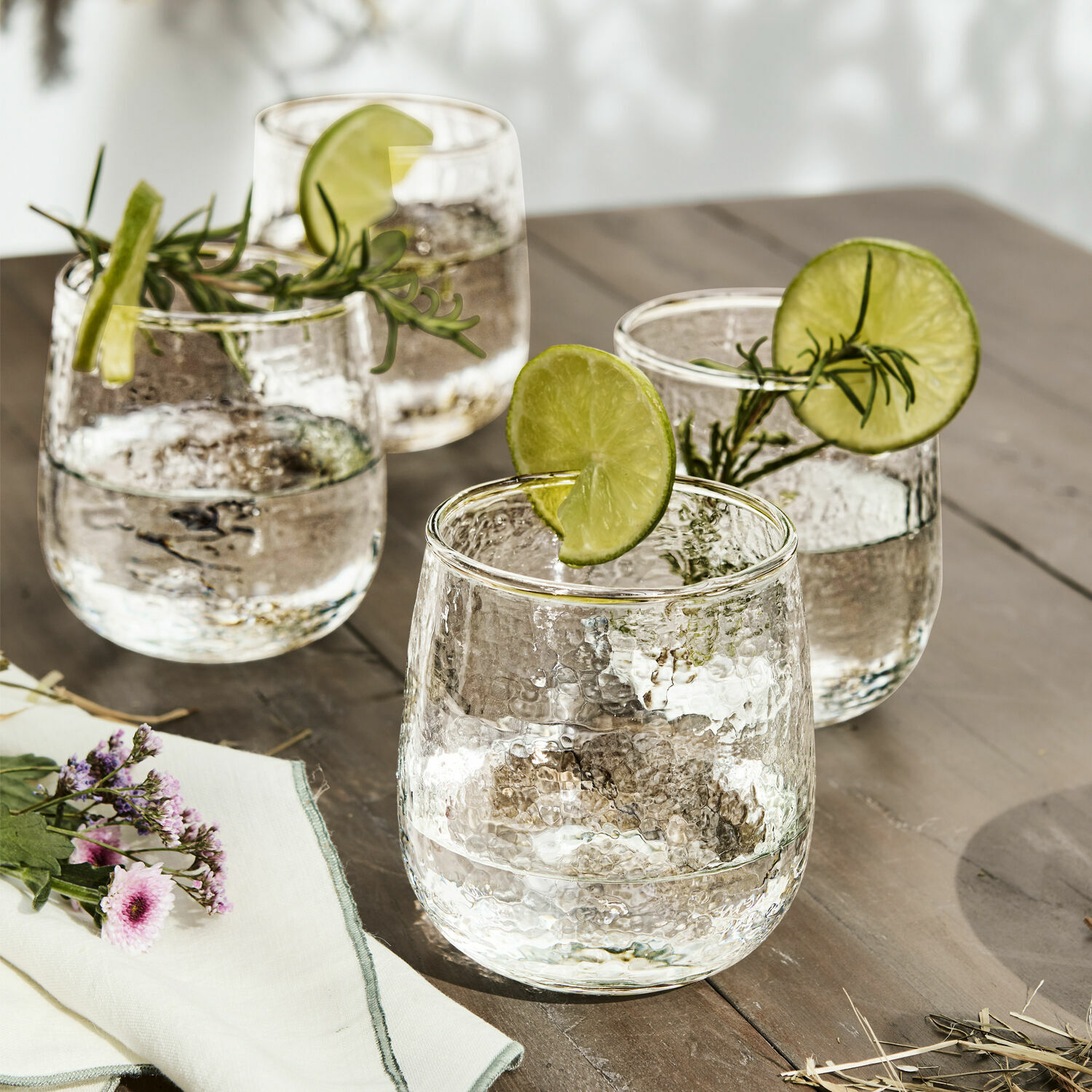 Glas 4er Set Valters Vier Gläser aus gehämmertem Glas mit Limettenscheiben und Rosmarinzweigen auf Holztisch