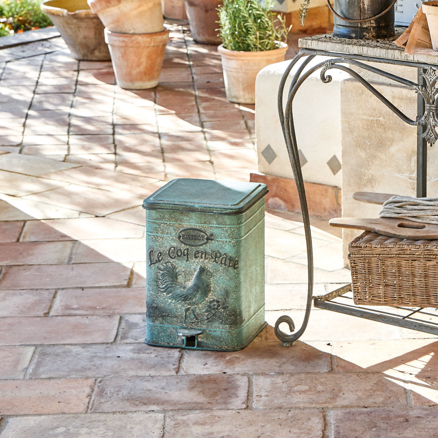Grüner Metall-Abfalleimer mit Hahn-Motiv auf Terrasse mit Ziegelboden, rustikaler Stil