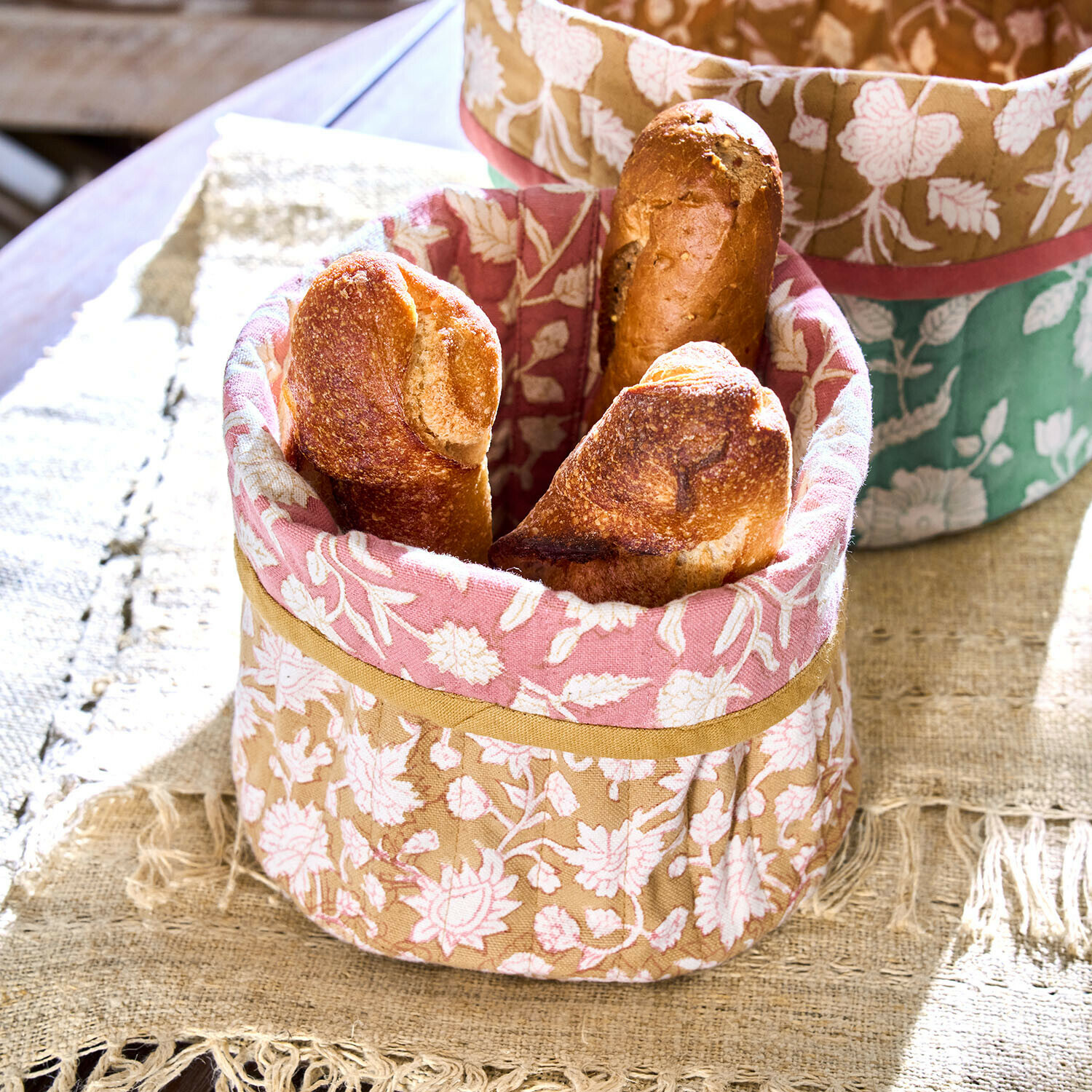 Baumwollkorb in Beige-Rosa mit Blumenmuster, gefüllt mit knusprigen Baguettes auf Tisch