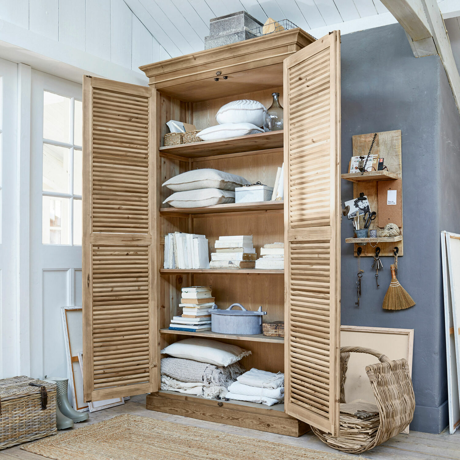 Holzschrank mit Lamellentüren in Naturfarbe, gefüllt mit Büchern und weißen Textilien