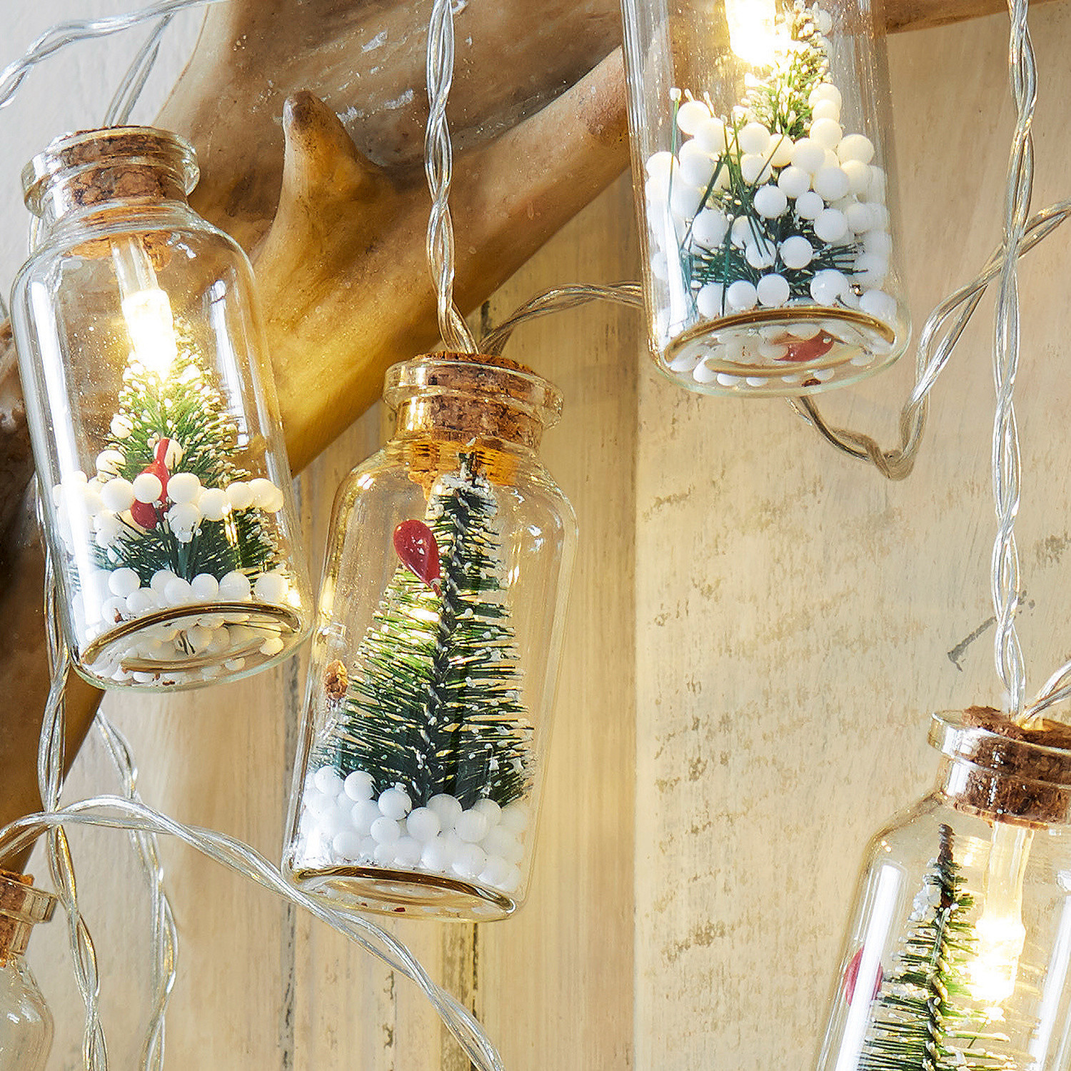 Lichterkette mit kleinen Glasfläschchen, grünen Tannenbäumen und weißen Schneebällen als Dekoration