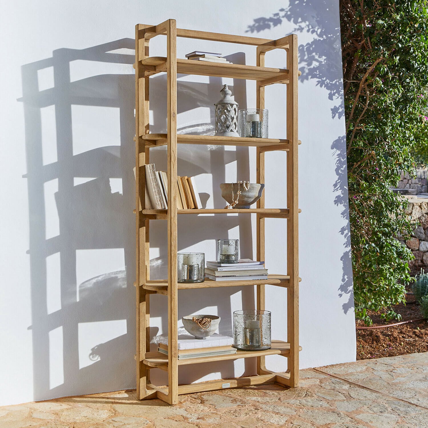 Regal aus natürlichem Teakholz mit Dekorationen und Büchern im Außenbereich bei Sonnenschein