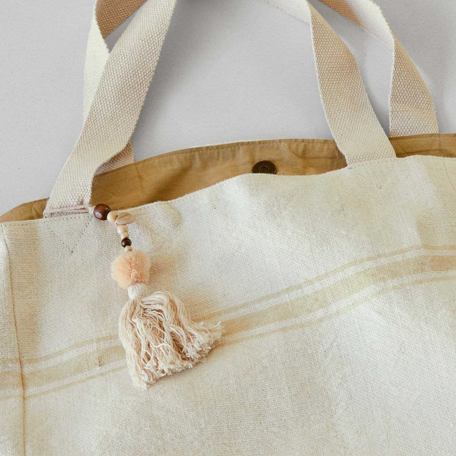 Beige Stofftasche mit dekorativem Quastenanhänger und Holzperlen, praktischer Alltagsbegleiter