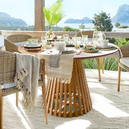Runder Teakholztisch mit Korbstühlen und sommerlicher Tischdeko auf Terrasse mit Meerblick