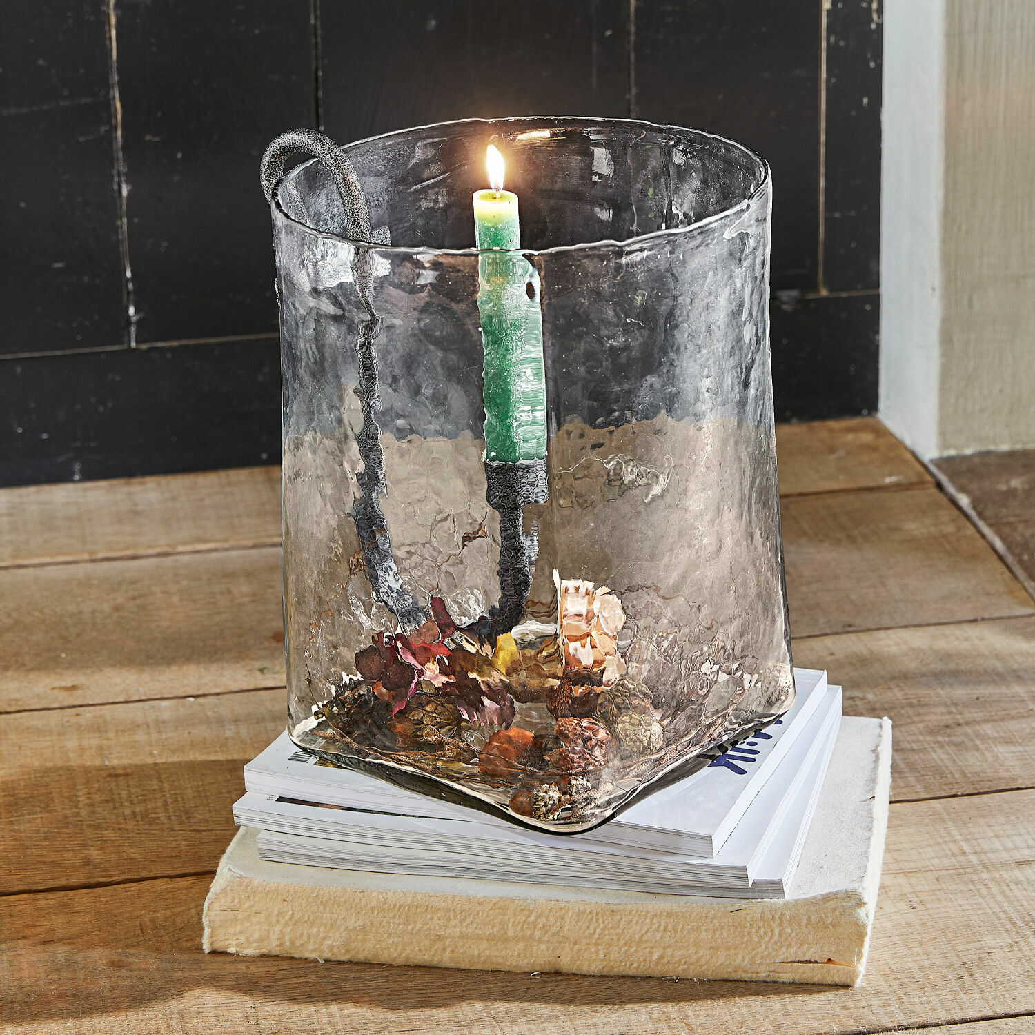 Glas-Kerzenhalter mit Metallgriff und grüner Kerze auf Holztisch mit Zapfendekoration