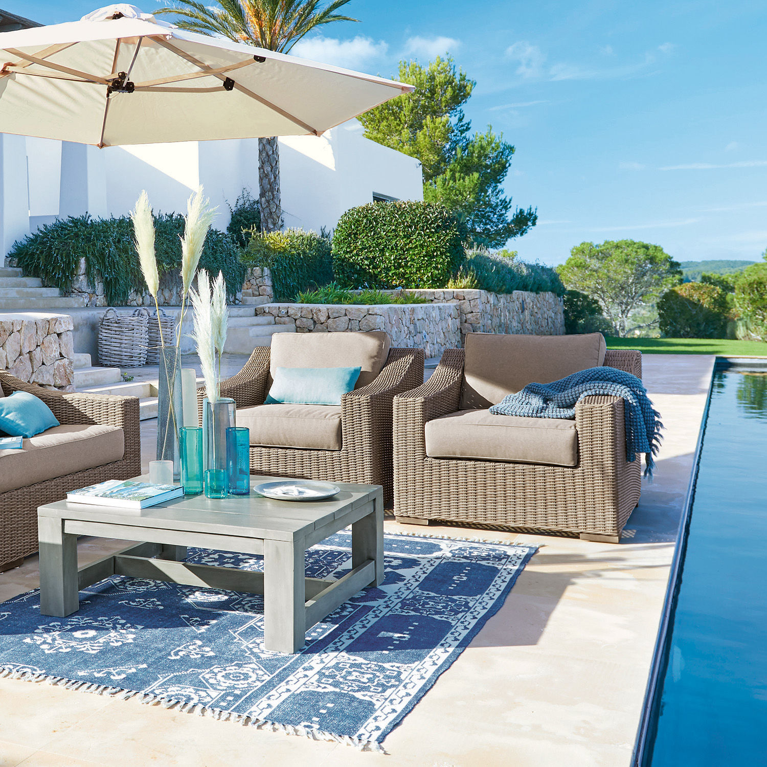 Gartenmöbel-Set mit beigen Polstern und grauem Tisch auf blauem Teppich neben dem Pool