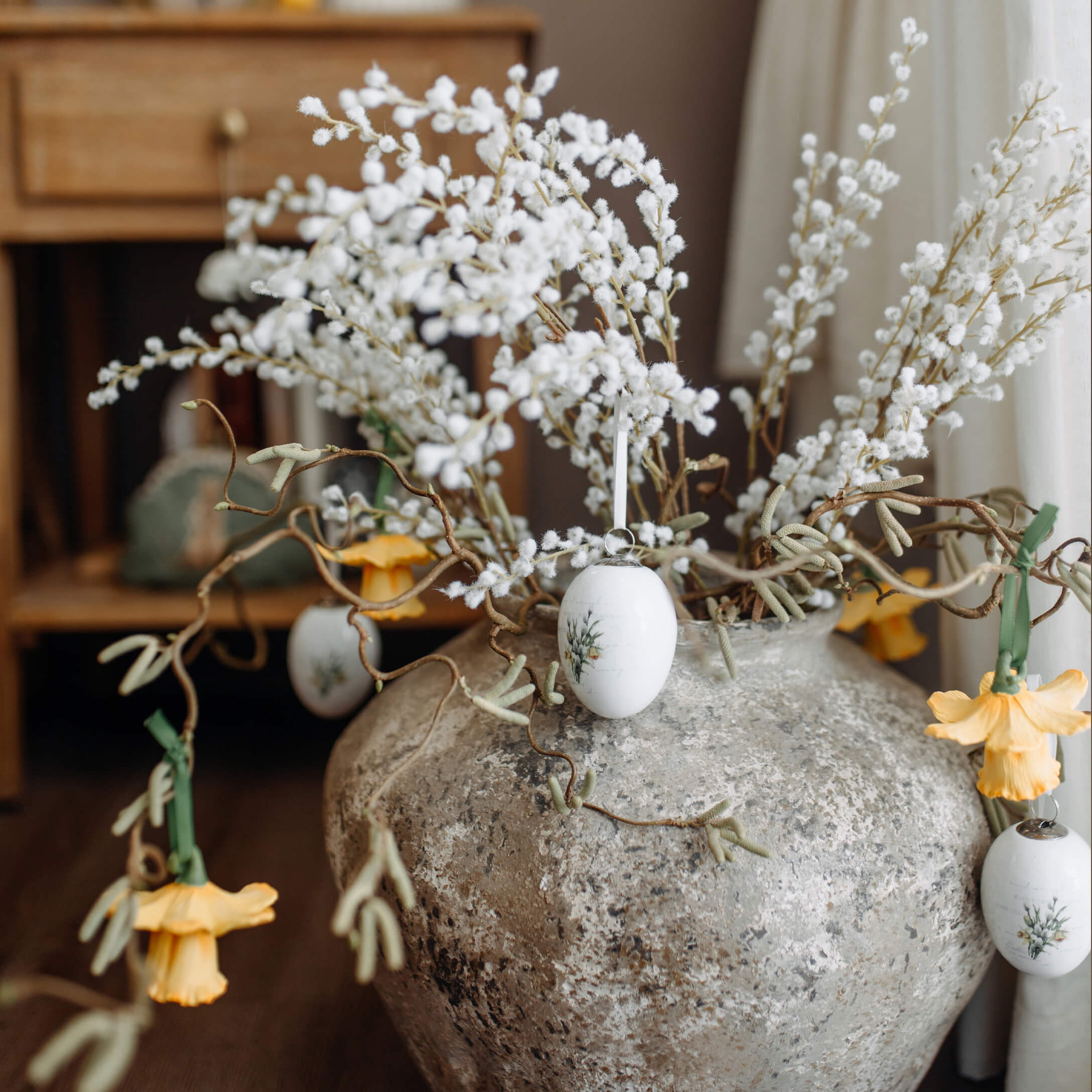 Großer grauer Steinvase mit weißen Zweigen und gelben Blumen als Osterdekoration im Raum