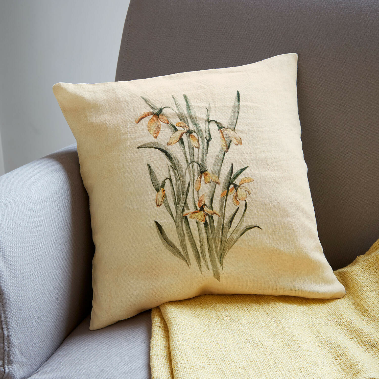 Kissenhülle Lozere Beiges Leinenkissen mit gelbem Blumenmotiv auf grauem Sofa und gelber Decke