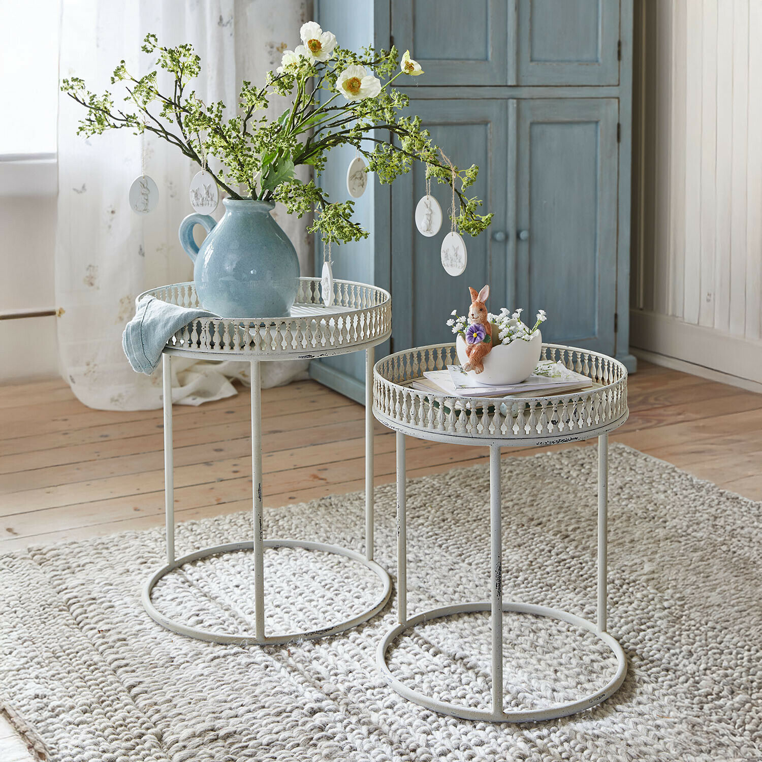 Beistelltisch 2er Set Vireline Zwei weiße Metall-Beistelltische mit filigranem Rand auf grauem Teppich, dekoriert mit Vase und Hasenfigur