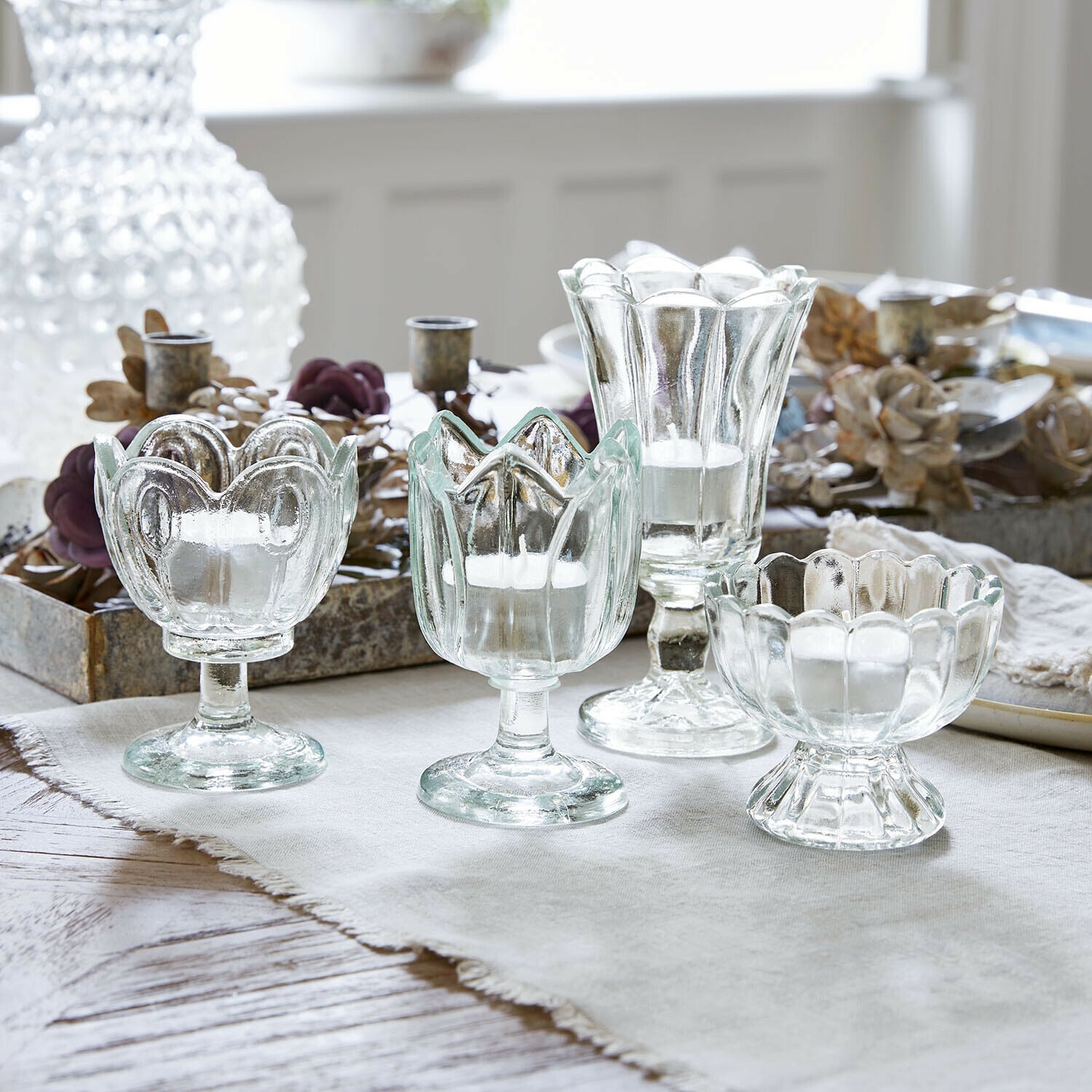 Windlicht 4er Set Amisette Set aus vier transparenten Glas-Teelichthaltern in verschiedenen Formen auf hellem Tuch